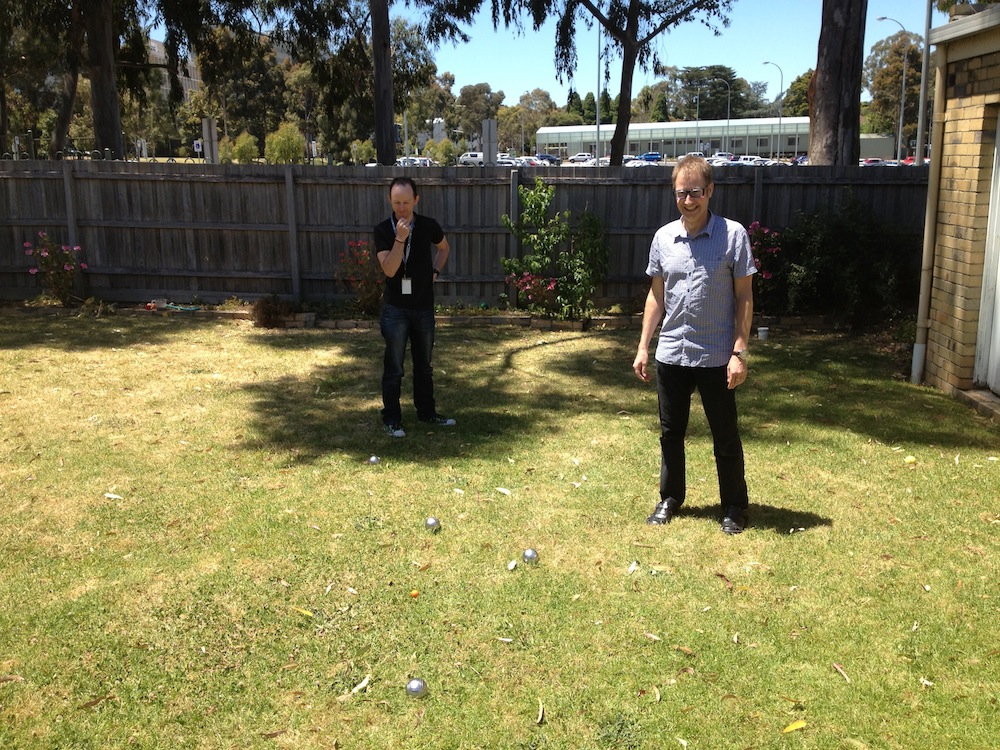 Matt and Kim observing Pétanque, with a view of the Monash Campus in the background.